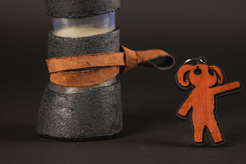 Textured water bottle holder with a leather strap, and a wooden keyring featuring a character design.