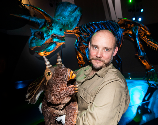 A man poses with a baby triceratops in front of Horridus, the triceratops fossil found at Melbourne Museum.