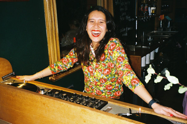 DJ Sweetie stands over a vinyl DJ deck smiling