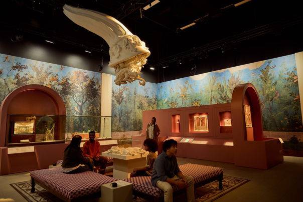 People sitting and standing chatting in the middle of ROME: Empire, Power, People exhibition in Melbourne Museum.