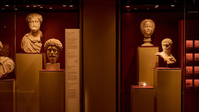 Display case of Roman marble busts arranged on plinths against deep red gallery walls. 
