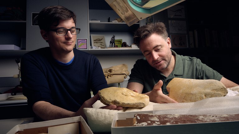 two men holding yellow coloured fossil bones in a laboratory