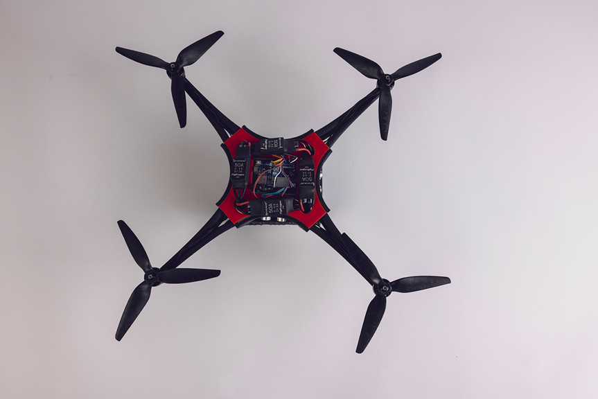 Quadcopter drone with black and red frame and exposed electronics, viewed from above.