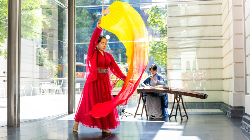 A performer in a long red dress is dancing with a bright purple ribbon fan. 