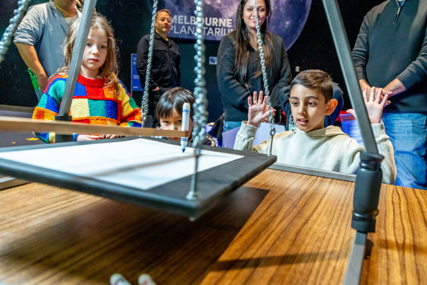Child using a harmonograph during Science is a Superpower festival at Scienceworks.