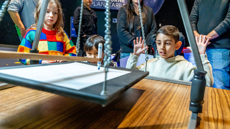 Child using a harmonograph during Science is a Superpower festival at Scienceworks.