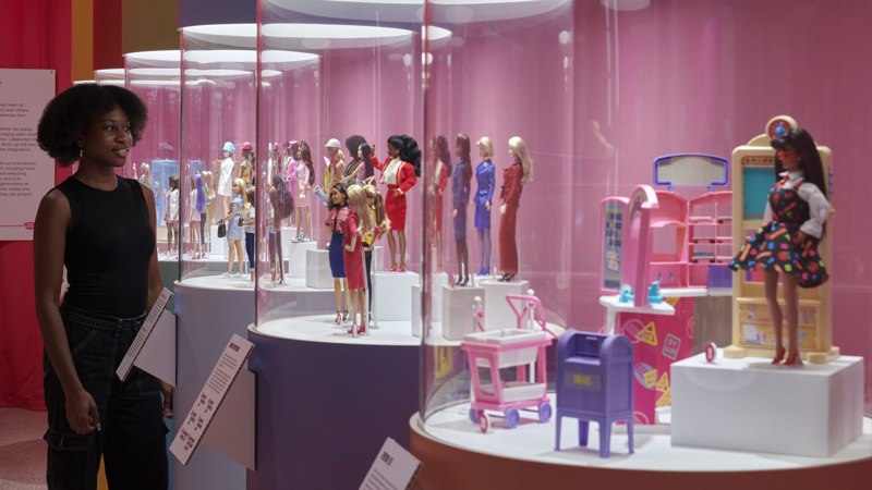 Barbies with accessories in clear, tube shaped displays.