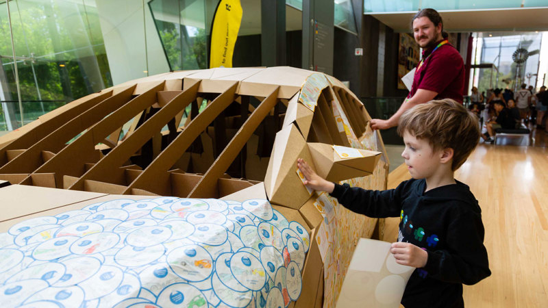 A child places stickers on a life-size cardboard car.