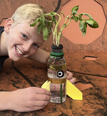 Boy smiling with a basil plant growing in a bottle.