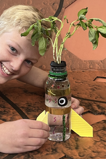 Boy smiling with a basil plant growing in a bottle.