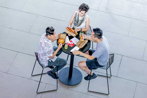 Three people sit at table and eat burgers and hotdogs