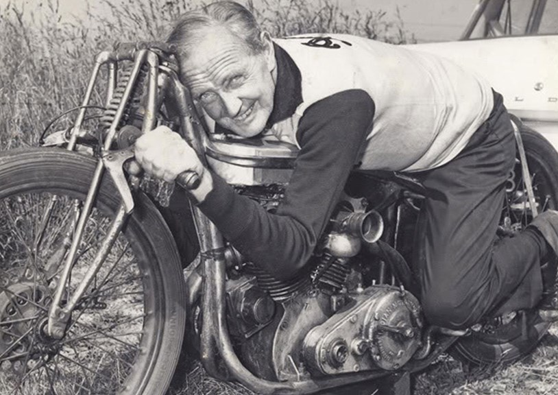 A black and white photo of a man straddling a motorcycle
