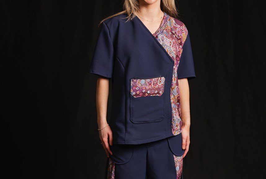Person wears a navy blue medical uniform that features striking pink artwork on the pockets and side panels.