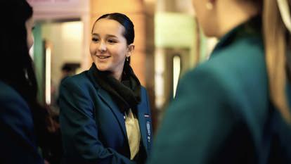 Three high school students in school uniforms, talking to each other in a gallery at the Immigration Museum.  
