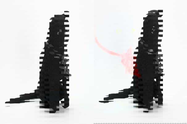 Large, almost life-size, toy cat. Made from a black knitted synthetic fabric, with green glass eyes, grey embroidered nose and mouth, and frayed red ribbon around its neck.