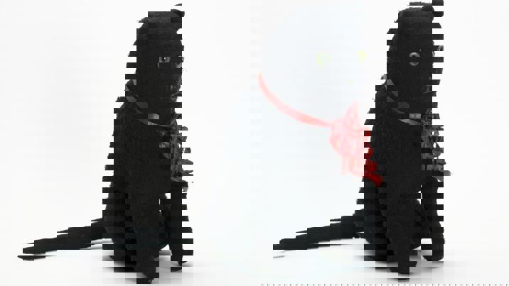 Large, almost life-size, toy cat. Made from a black knitted synthetic fabric, with green glass eyes, grey embroidered nose and mouth, and frayed red ribbon around its neck.