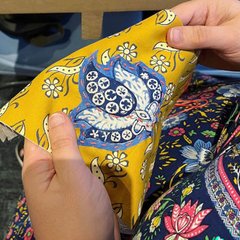 A person holding a piece of yellow floral fabric with a blue embroidery on it.