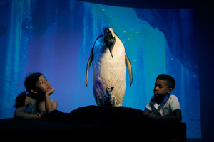 Two children standing either side of a taxidermy model of an Emperor Penguin (Aptenodytes forsteri).