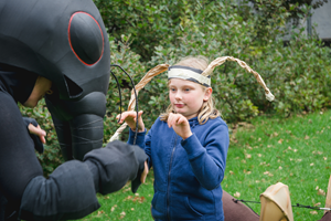 A child wearing a head band with antennae imitates the pose of one of the worker ants.