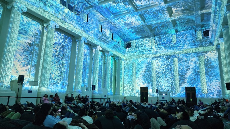 People watching a lightshow projected on the walls of the Long Room at the Immigration Museum.