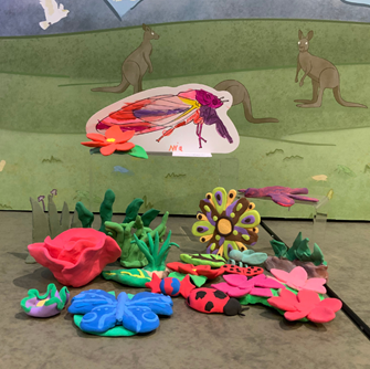 A cicada coloured illustration sits next to a plasticine bugs and flowers in a close-up of a bugs themed Diorama.