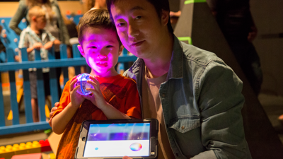 A parent and child hold an ipad showing the on-screen controls used to control sphero robts.