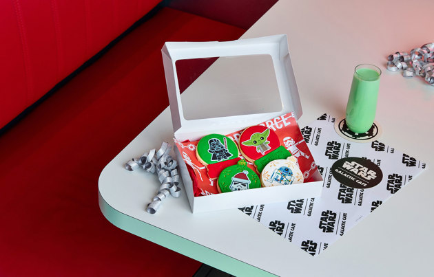 A box of four star wars cookies next to a glass of green milk.