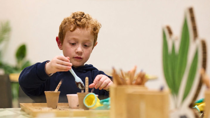 Child planting seeds in small pots during a hands-on museum learning activity.
