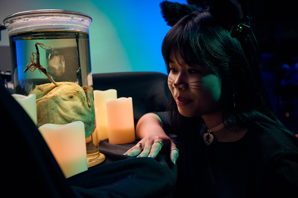 A woman in a cat costume inspects an Anglerfish in a jar.