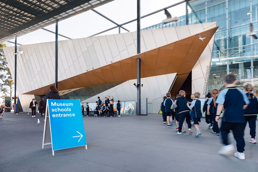 A school group walks into Melbourne Museum’s schools entry, there is a sign out saying ‘Museums schools entrance’. 