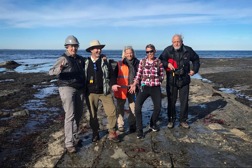 Five people posing for a photo on a rocky beach