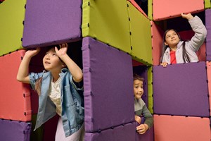 Children playing games in a cubby house they have built together out of multi-coloured cushions.