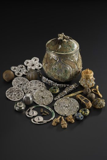 A collection of Viking-era treasures known as the Galloway Hoard, including ornate silver metalwork and lidded vessel displayed against a black background