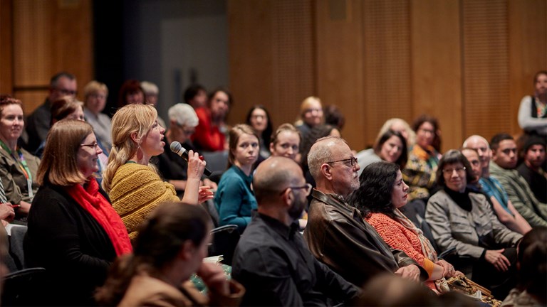 A woman holding a microphone asks a question from the audience of the Melbourne Museum Theatre.
