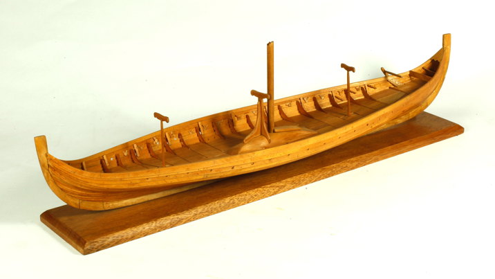 A wooden scale model of a Viking longship displayed on a wooden base, featuring a single central mast.