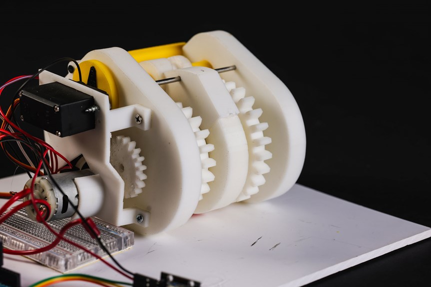 Close-up view of white plastic gears attached to red wires and arduino.