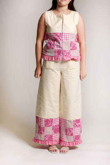 Model wearing a cream-coloured sleeveless top and wide-leg trousers with pink patchwork panels featuring gingham and floral patterns, finished with a pink, ruffled trim.