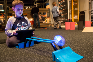 A child using an iPad to control a sphero robot up a ramp and onto parallel ball tracks.