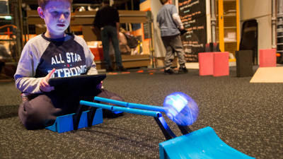 A child using an iPad to control a sphero robot up a ramp and onto parallel ball tracks.