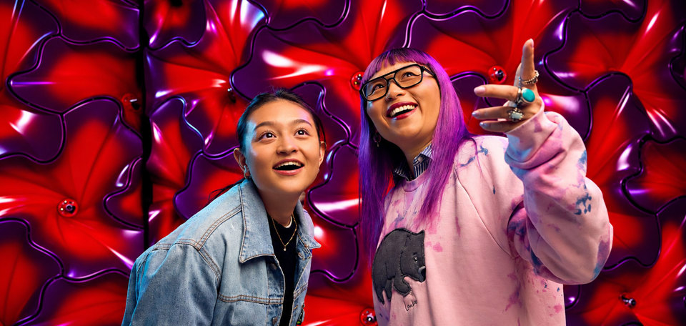 Two happy museum visitors standing in front of a neon petal wall.
