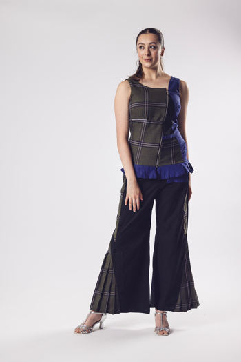 Person in a tartan and pleated sleeveless top with coordinated trousers and silver heels stands against a white background.
