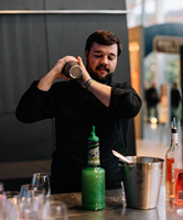 A bar-person prepares a cocktail in a shaker.