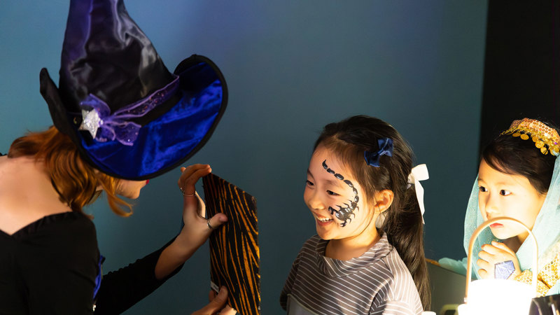 A little girl smiles with enjoyment as she is shown the painted scorpion on her face during Halloween at the Museum.