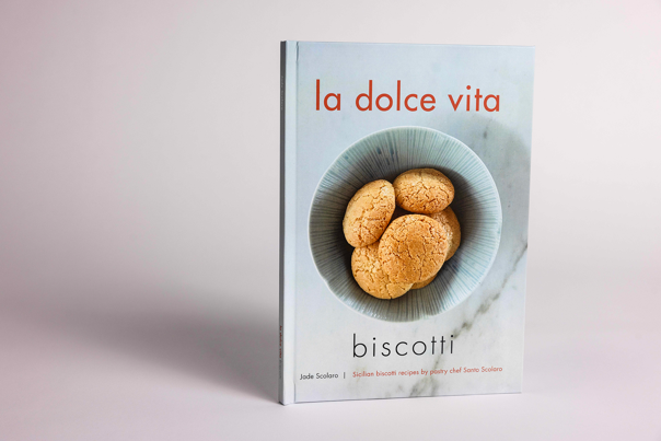 Hardback recipe book whose cover features a round bowl of biscotti, on a marble surface.
