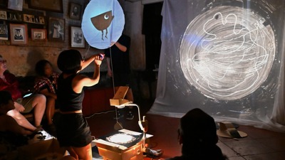 Artist Youbi Lee manipulates black cardboard shapes to bring her shadow puppet performance to life.