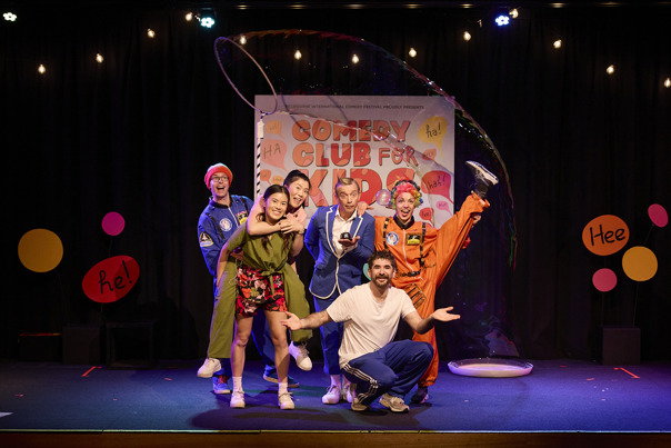 A group of 6 performers posing on the stage of the kids comedy club.