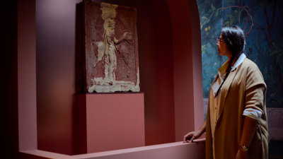 Visitor standing beside a carved stone relief set within a curved, terracotta-colored exhibition display. 