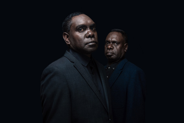 David And Daniel Wilfred in blue suits on a dark black background.