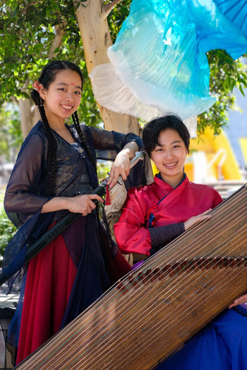 Madison and QiQi posing for a photograph. Madison is standing and holding a sword, and QiQi is sitting with a guzheng.