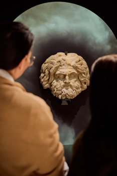 A couple people looking at a large stone statue head of a roman god in ROME: Empire, Power, People exhibition in Melbourne Museum.